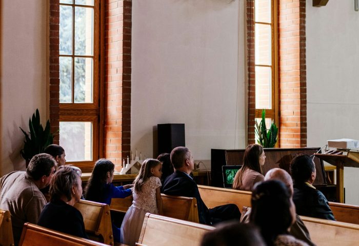 People sitting in wooden pews inside a church, attentively listening during a service or gathering.