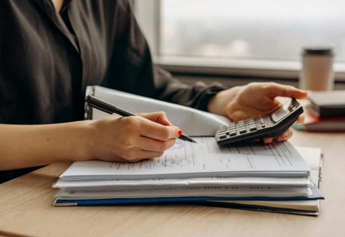 Person using a calculator and writing on financial documents at a desk, representing accounting or financial work.