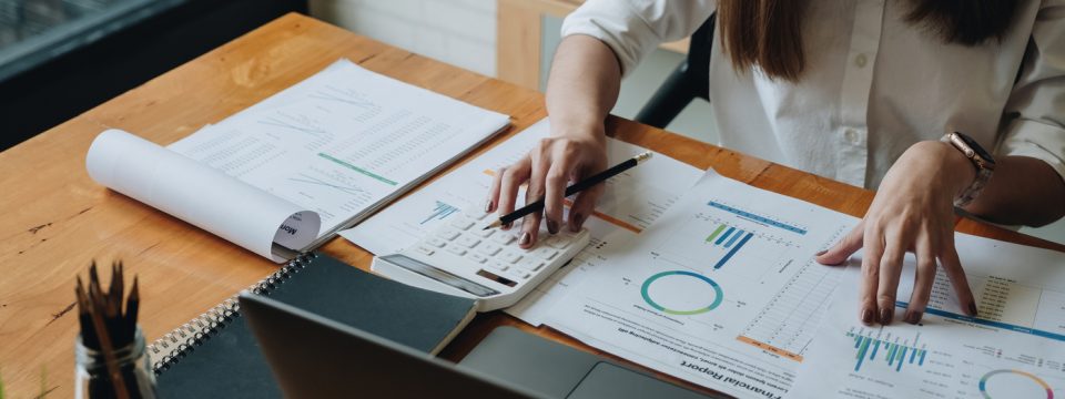 Person analyzing financial charts and using a calculator at a desk with reports and a laptop, representing financial planning.