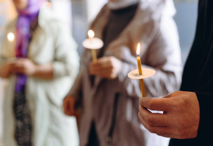 People holding lit candles during a vigil or ceremony, with a focus on hands and glowing candle flames.