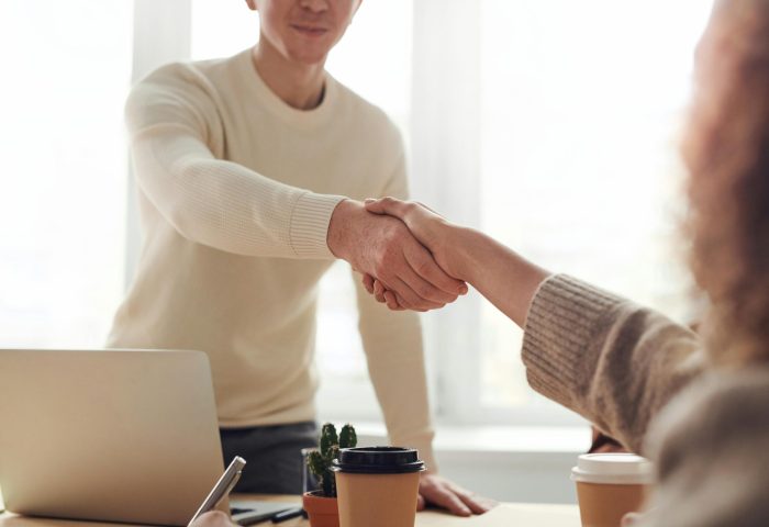 Two people shaking hands in an office setting, symbolizing agreement, partnership, and collaboration.