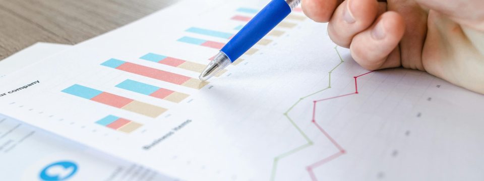 Person holding a pen and analyzing bar and line graphs on financial documents, representing data analysis or reporting.